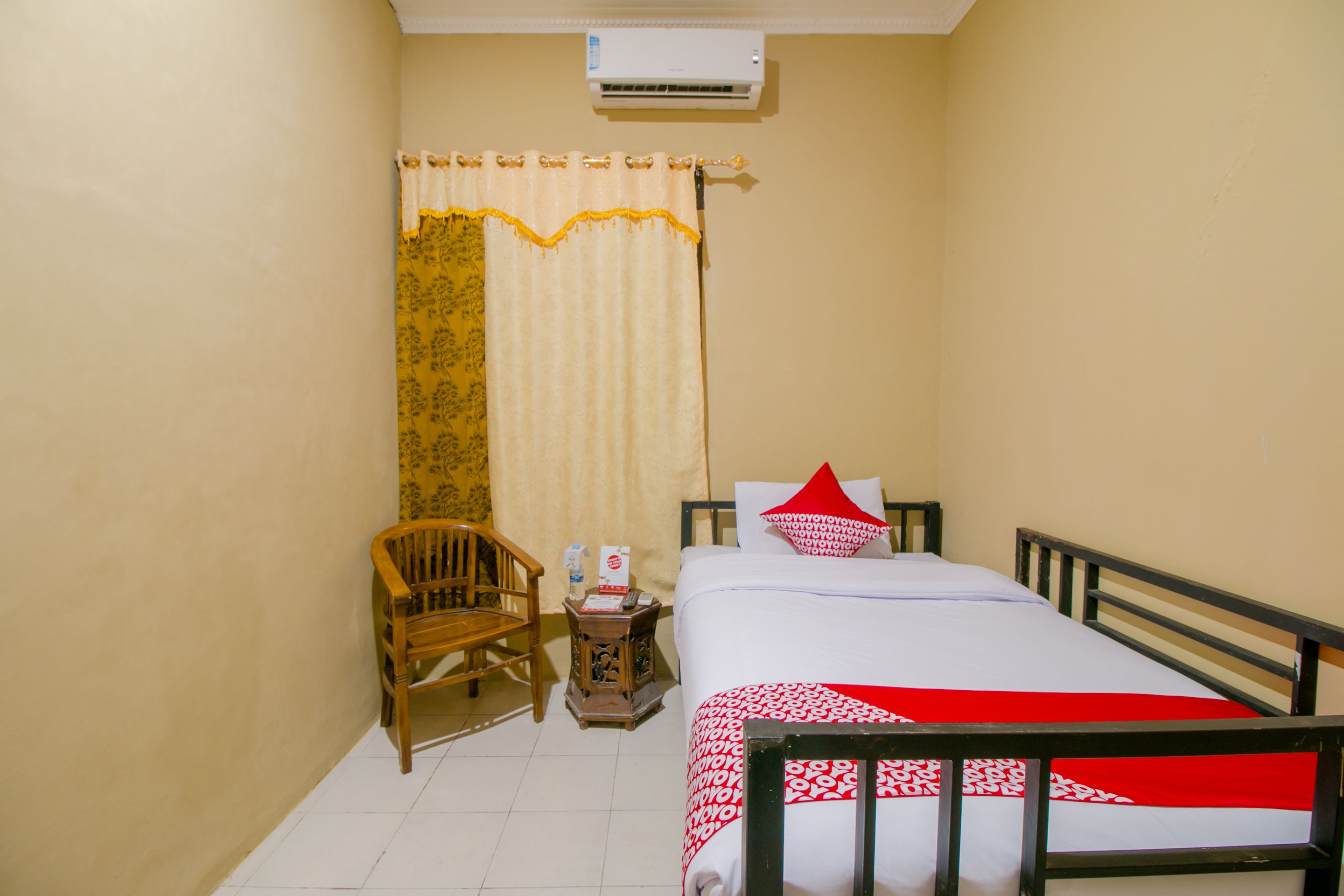 A bedroom with a bed, a chair, a nightstand, and an air conditioning unit.