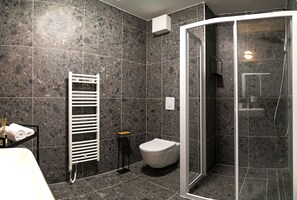 Un baño moderno con ducha envuelta en vidrio, un inodoro blanco y un perchero con toallas.