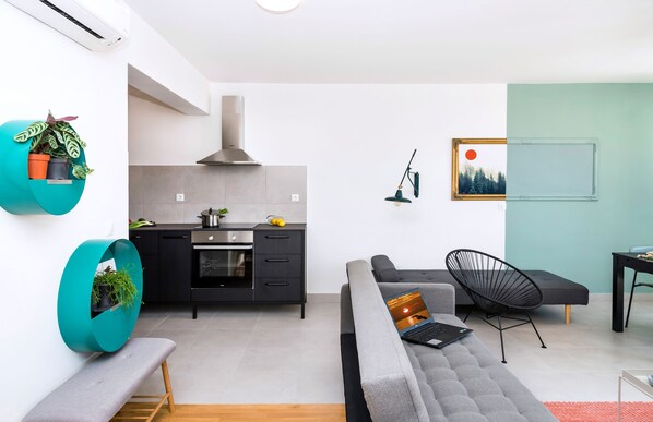 A modern living space with a kitchen, a grey sofa, a black chair, and a bench.