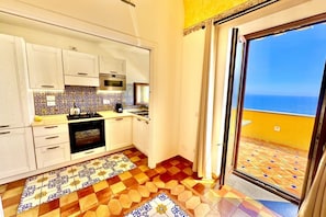 Una cocina con armarios blancos, una estufa y vistas al mar a través de un ventanal corredero.