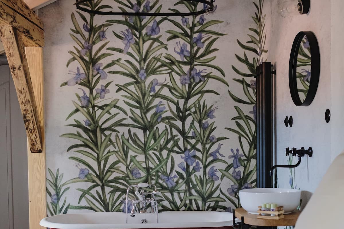 Un dormitorio con una bañera roja, techo de madera y papel tapiz floral.