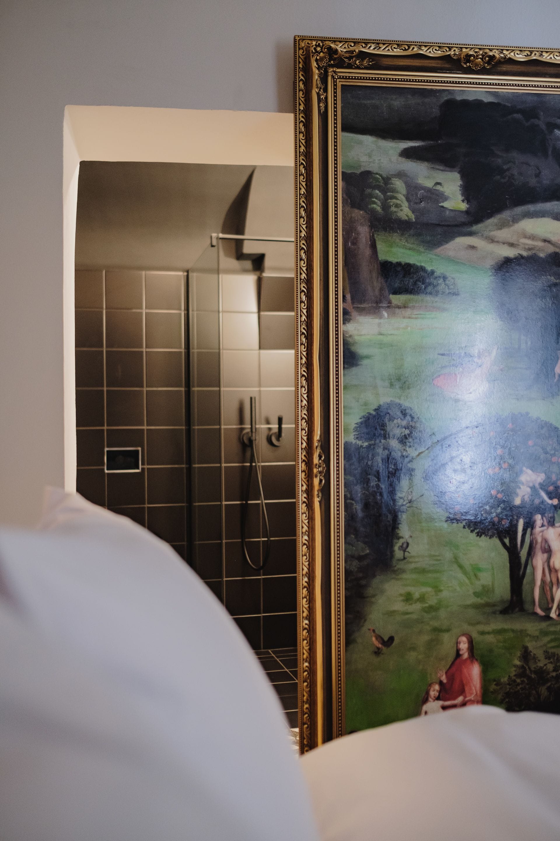 A bathroom with a shower and a framed painting of a pastoral scene.