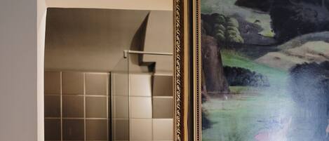 A bathroom with a shower and a framed painting of a pastoral scene.