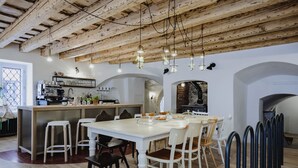 Un comedor con una mesa y sillas blancas, una cocina al fondo y un techo de madera rústica.