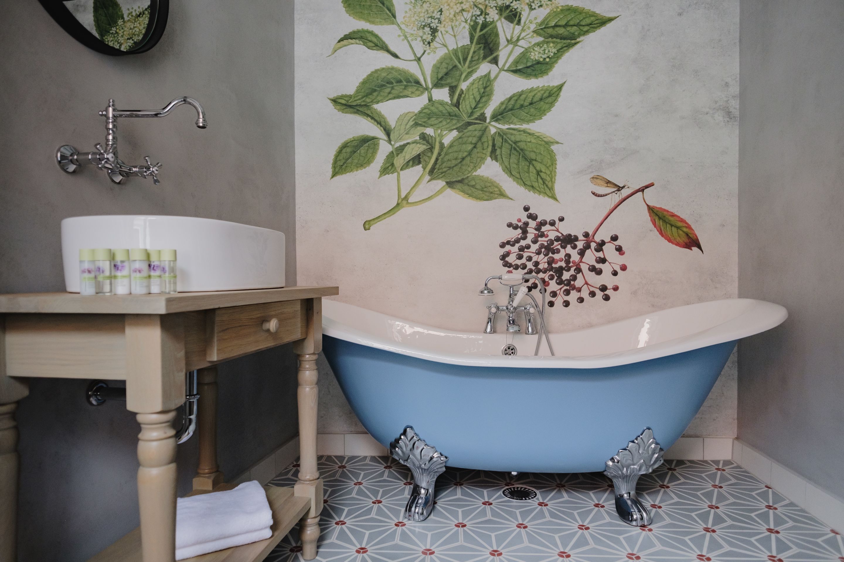 Un baño con una bañera azul tipo pata de león, un tocador de madera con lavabo y un espejo montado en la pared.