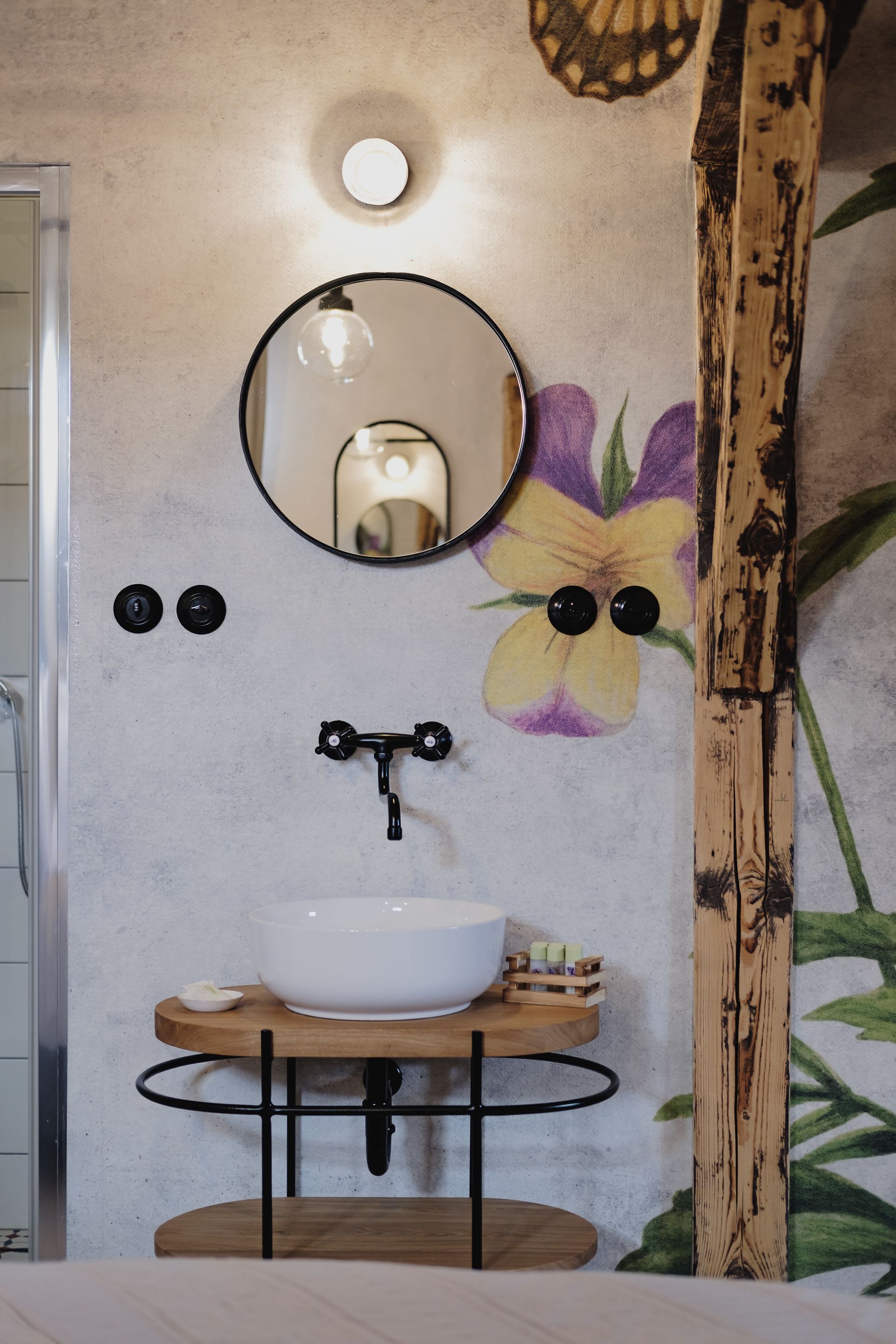 A bathroom with a white sink, a round mirror, and a floral wall mural.