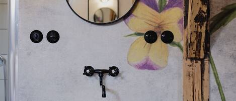 A bathroom with a white sink, a round mirror, and a floral wall mural.