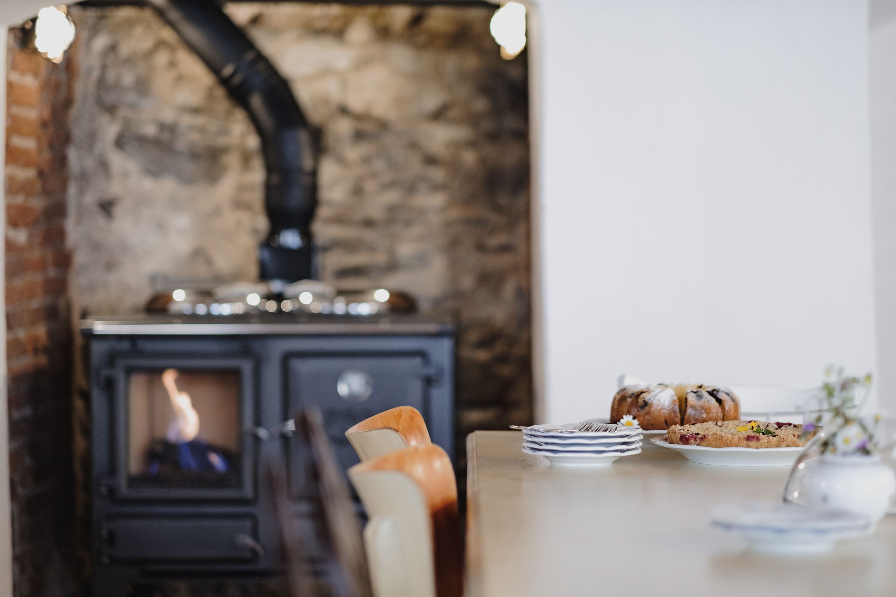 Une pièce chaleureuse avec un poêle à bois, une table à manger avec des assiettes et une miche de pain, et une chaise.