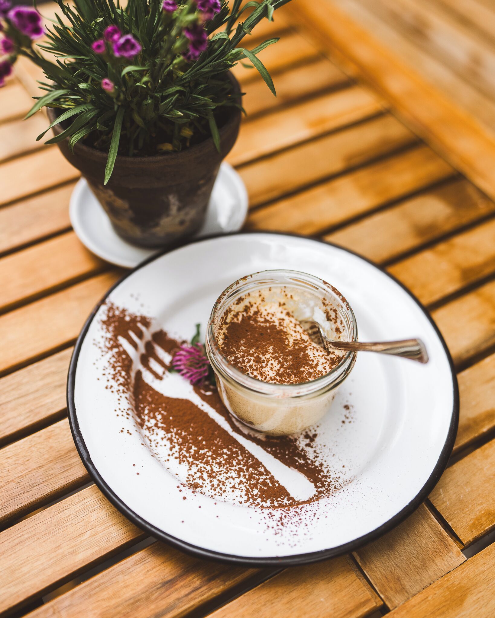 Dessert auf einem weißen Teller mit einem Löffel, bestäubt mit Kakaopulver, auf einem Holztisch.