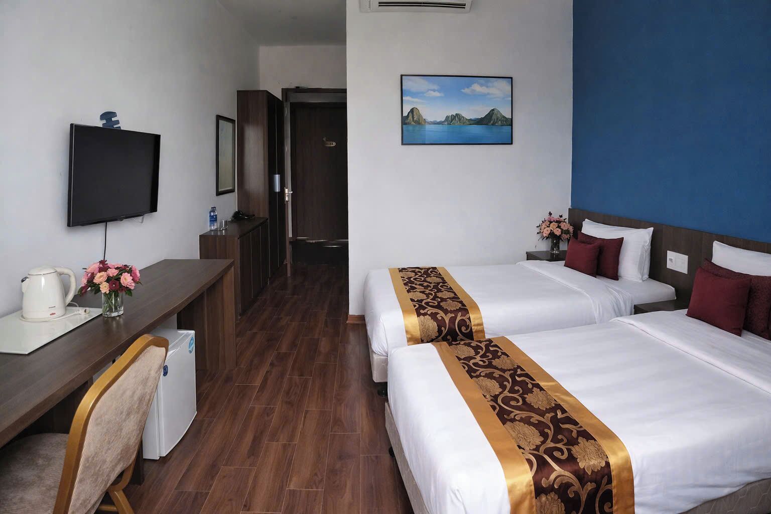 Ein Hotelzimmer mit zwei Betten, einem Schreibtisch, einem Fernseher und einem Landschaftsbild.
