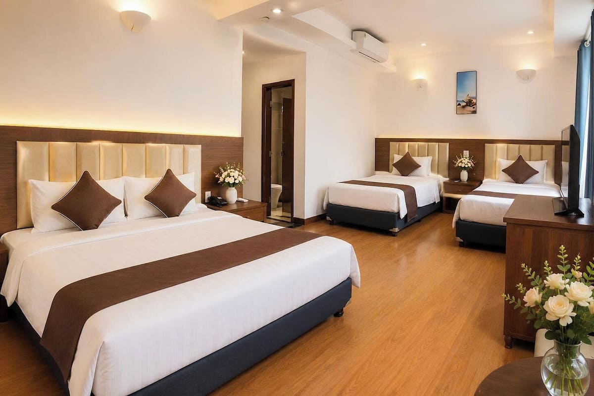A hotel room with three beds, a TV, a desk, and a vase with flowers.