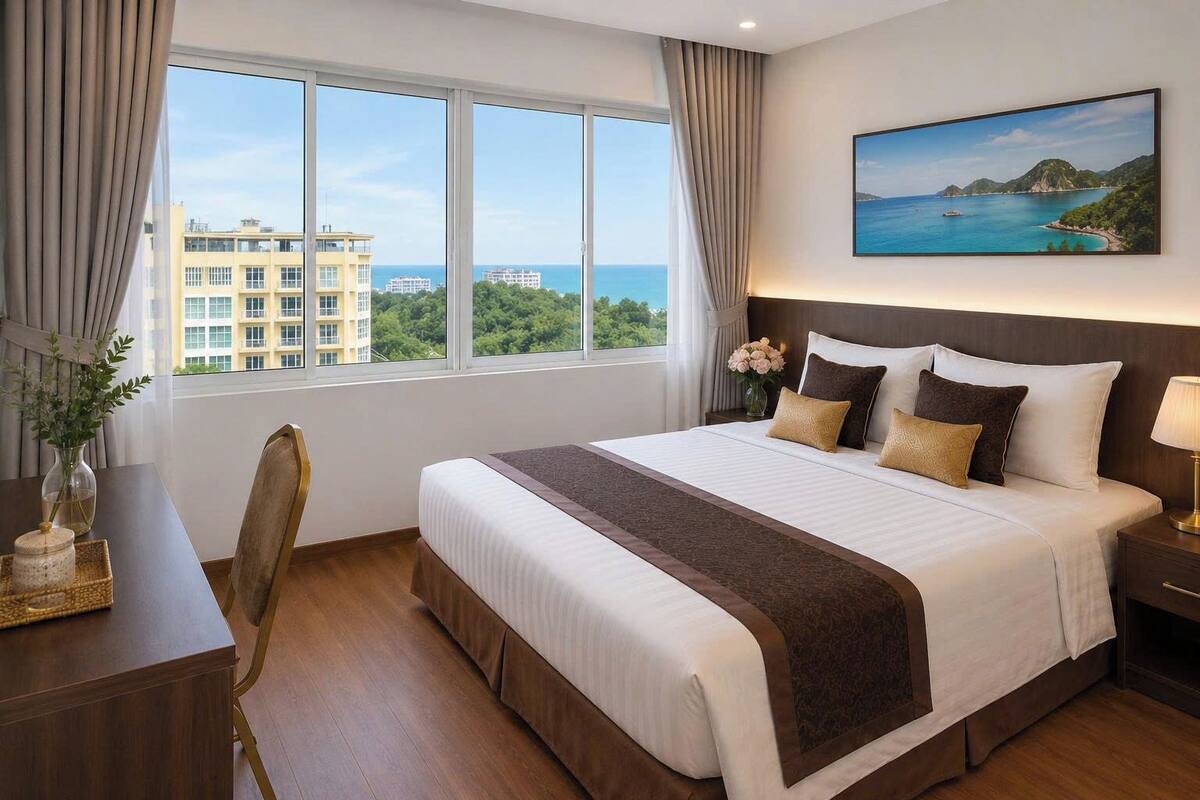 A hotel room with a large bed, a desk, a chair, a nightstand, and a painting of a coastal landscape.