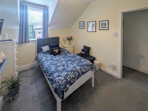 A bedroom with a bed, a nightstand, a small table with a vase, and a window with curtains.