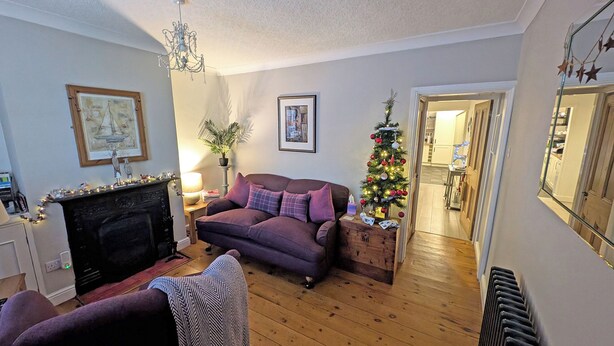 Ein Wohnzimmer mit Kamin, einer Couch, einem kleinen Weihnachtsbaum und einem Essbereich, der durch eine offene Tür sichtbar ist.