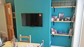 A room with teal walls, a wooden table with a remote control, a glass lantern, and a polka-dotted notebook. There are bookshelves with books and a clock. - 2 bedroom accommodation in Beverley (Beverley)