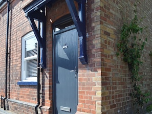 A brick house with a dark blue door, a window with blinds, and a small overhang above the door.