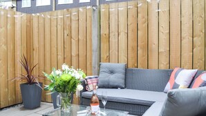 Eine Terrassenfläche mit einem Korbsessel, einem Glastisch und Topfpflanzen.