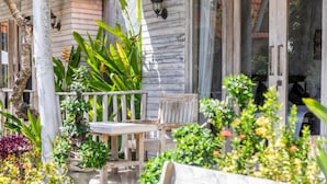 A wooden porch with a table and chairs, surrounded by lush greenery and a variety of plants. - The Box Paradise Bungalow (Penida Island)