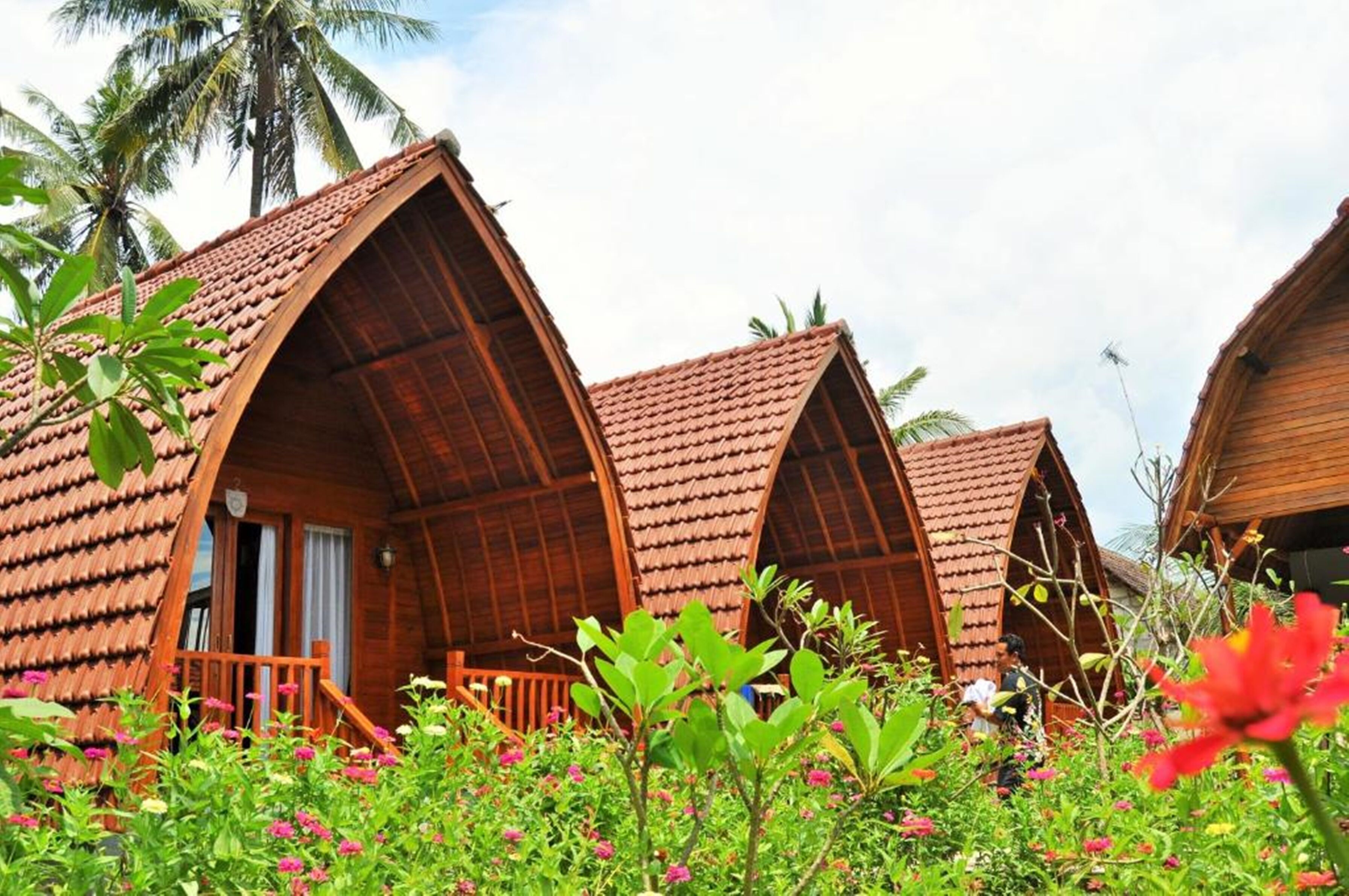 A row of wooden cottages with pitched roofs, surrounded by lush greenery and flowering plants.