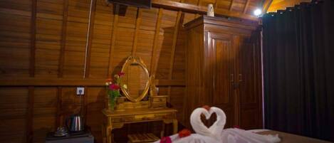 Une pièce en bois avec un lit, une armoire en bois, un miroir et une petite table sur laquelle se trouve un vase avec des fleurs.