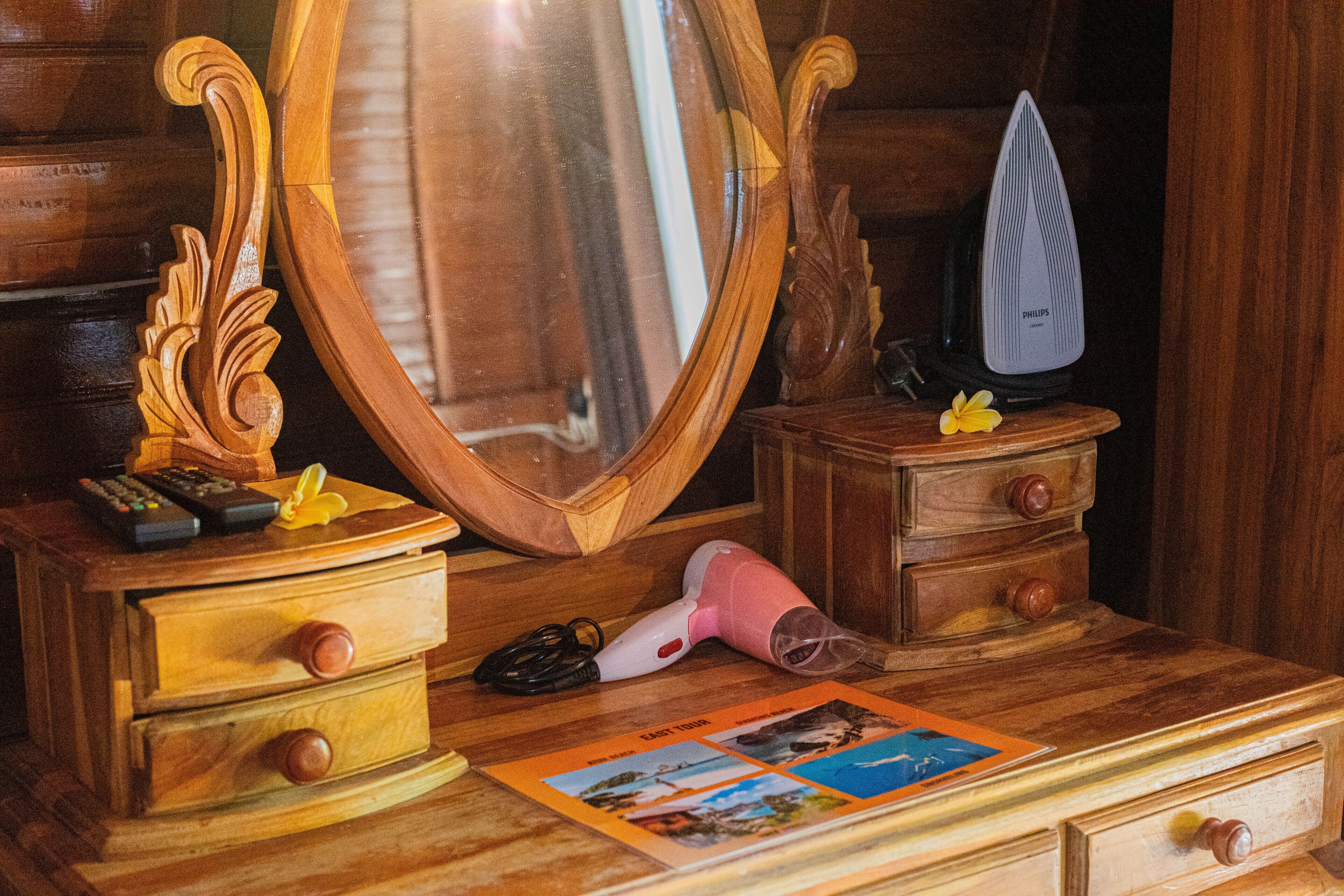 A wooden dresser with a mirror, a Philips hairdryer, a remote control, and a small drawer.