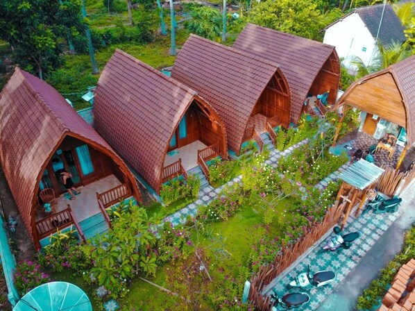 Un conjunto de cabañas de madera con techos inclinados, rodeadas de abundante vegetación y un sendero pavimentado.