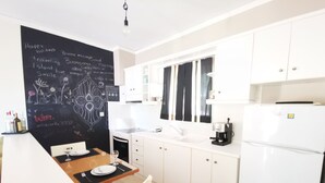 Una cucina moderna con mobili bianchi, una lavagna con frasi a tema viaggio, una macchina da caffè e un frigorifero.