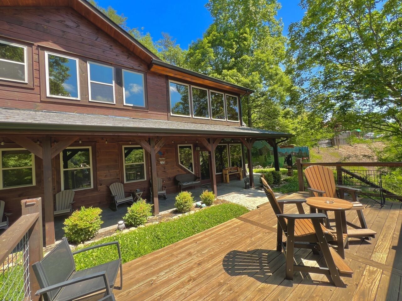 A two-story wooden house with a covered patio area featuring outdoor seating and a small garden.