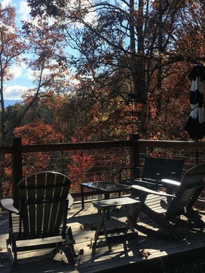 Une terrasse en bois avec des fauteuils Adirondack et une table, donnant sur une forêt aux couleurs automnales.