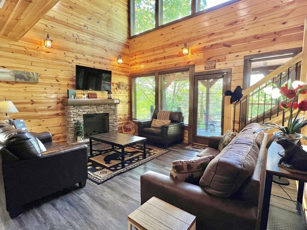 A log cabin interior with a fireplace, leather sofas, a dining table, and a staircase leading to an upper level.
