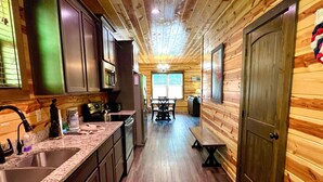 A wooden cabin interior with a kitchen, dining area, and a bench.