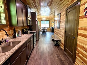 A kitchen with wooden walls, a granite countertop, and a dining area with a table and chairs. - South Side Serenity 2 Bedroom Cabin by RedAwning (Sevierville)