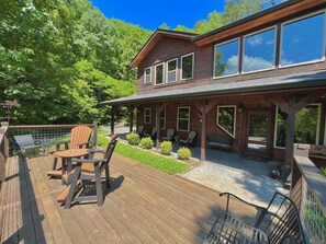 Une terrasse en bois avec des meubles d’extérieur, un patio couvert et une grande maison dotée de nombreuses fenêtres.