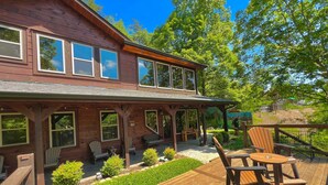 A two-story wooden house with a deck, outdoor seating, and a garden.