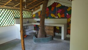 Une cuisine avec un tronc d’arbre central, un évier et un mur décoré de motifs colorés.
