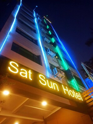 Une enseigne d’hôtel portant le nom « Sat Sun Hotel », illuminée en jaune.