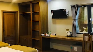 Habitación de hotel con un armario de madera, un escritorio con televisor de pantalla plana, una ventana con cortinas y una cama.