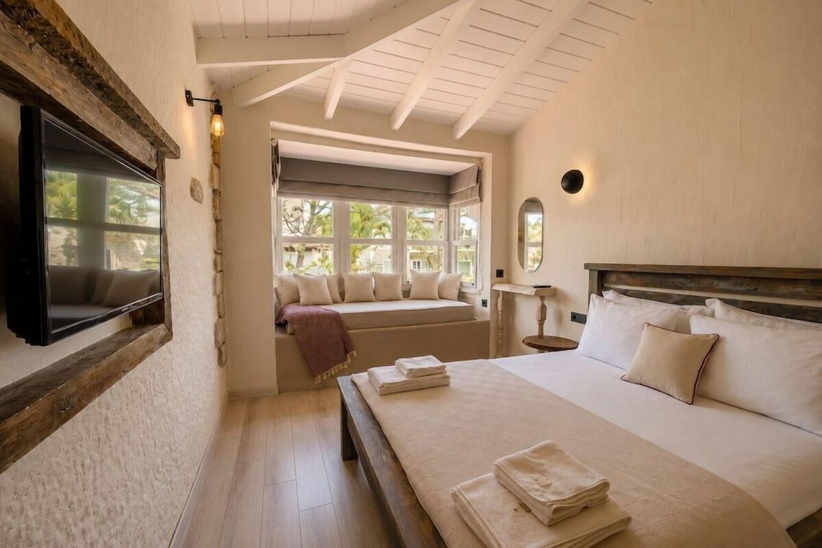 Un dormitorio con cama, un rincón con asiento junto a la ventana, televisión y vistas al exterior.