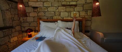 Una cama con ropa de cama blanca, un cabecero de madera y una pared de piedra.