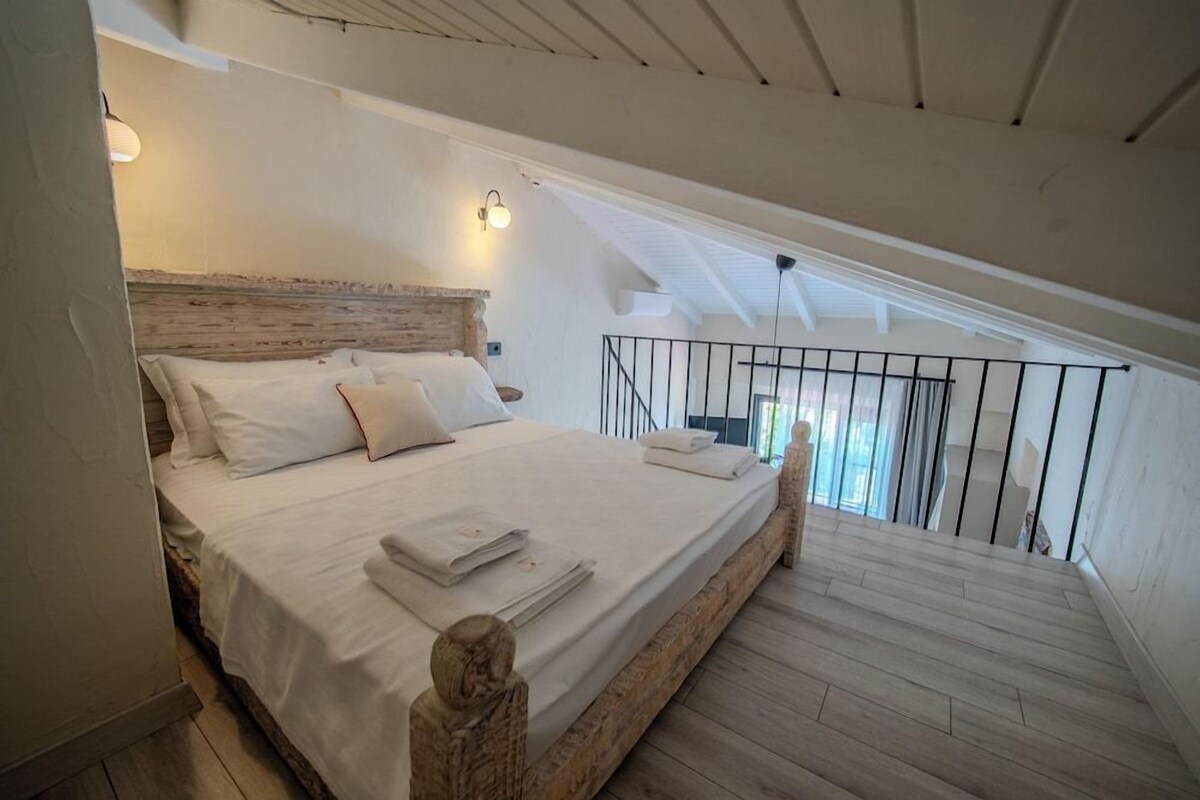 Un dormitorio con cama de madera, ropa de cama blanca y un balcón con barandilla.
