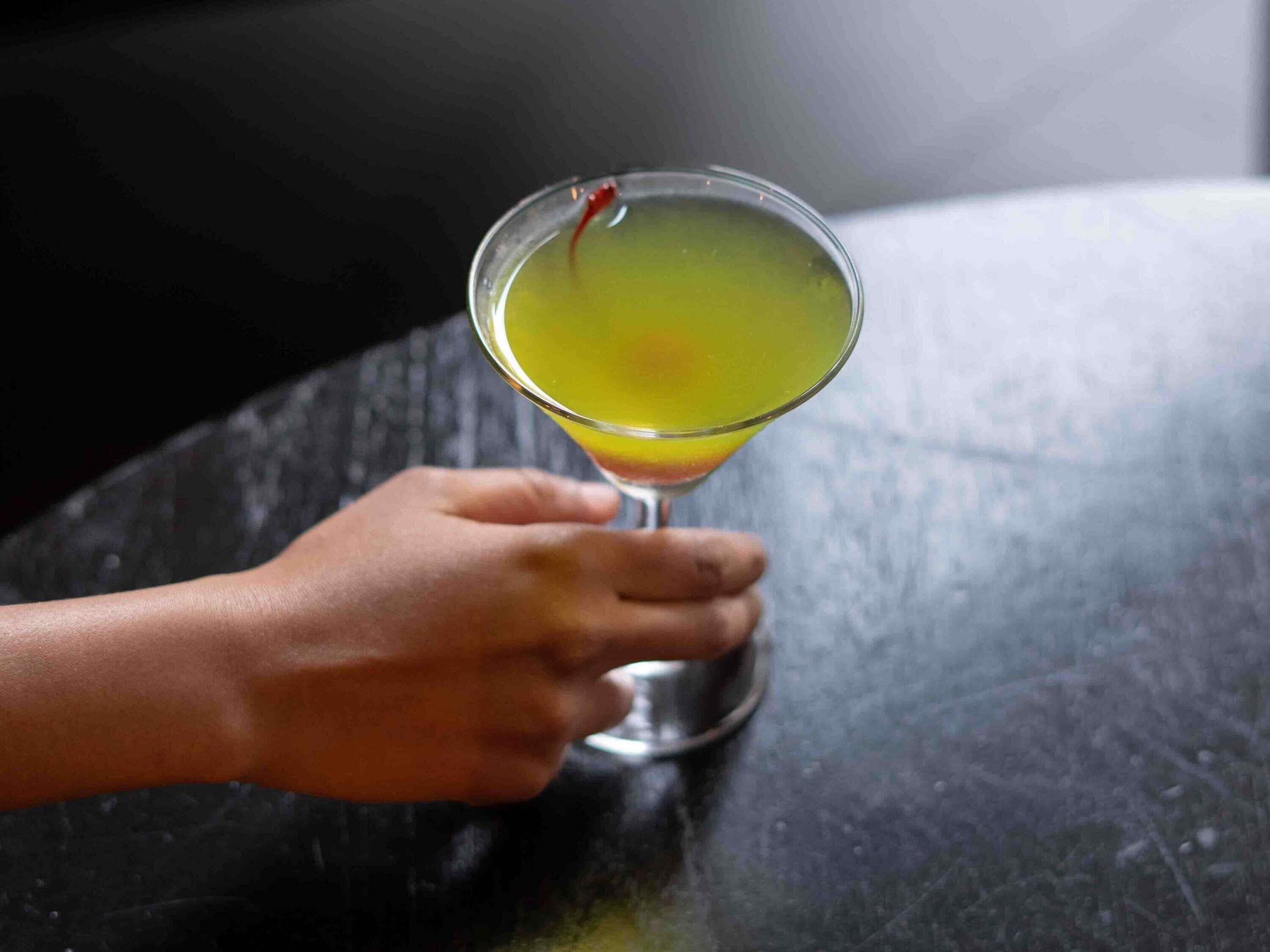 A hand holding a glass with a yellow liquid.