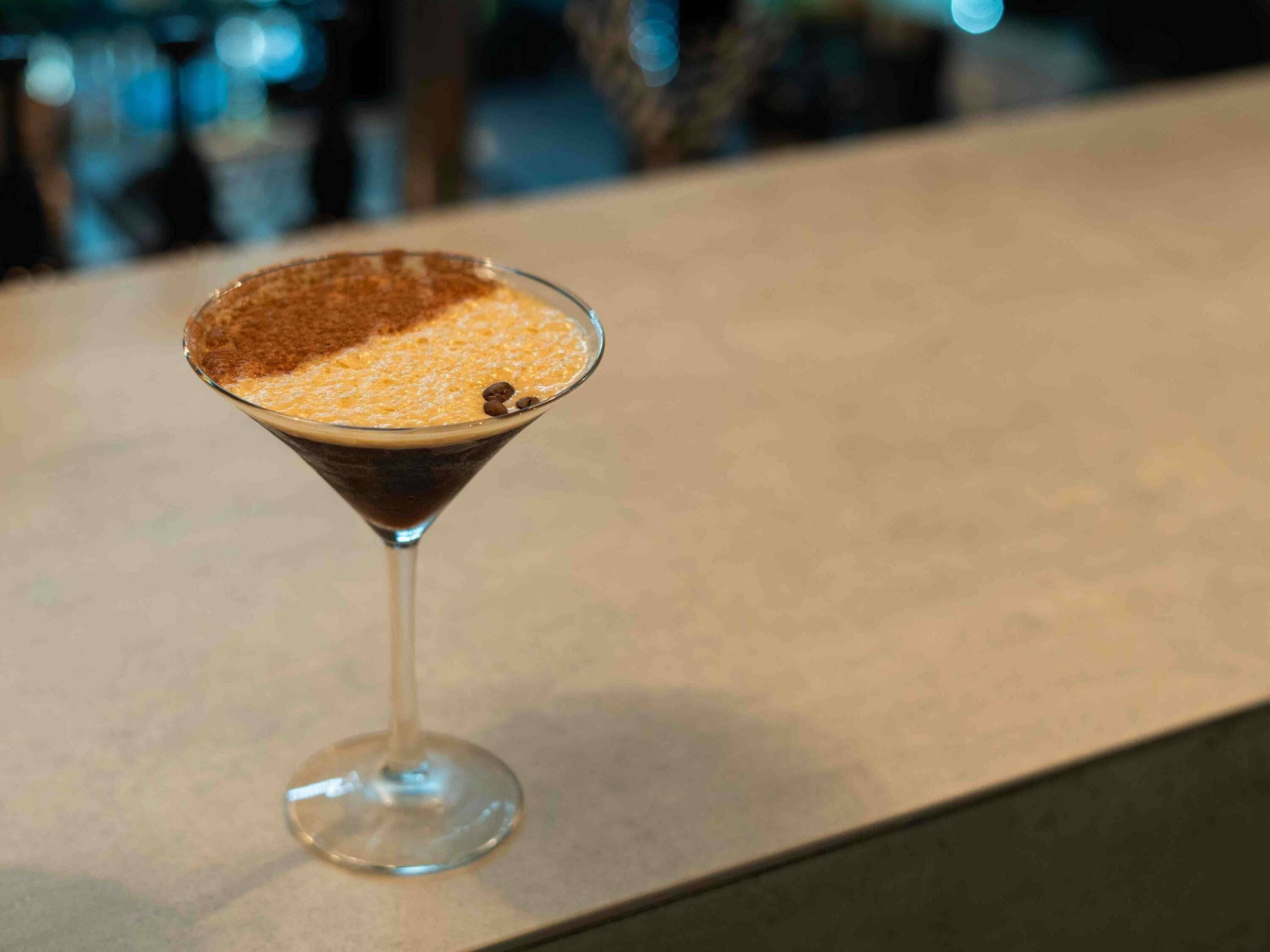 A martini glass with a frothy top on a bar counter.