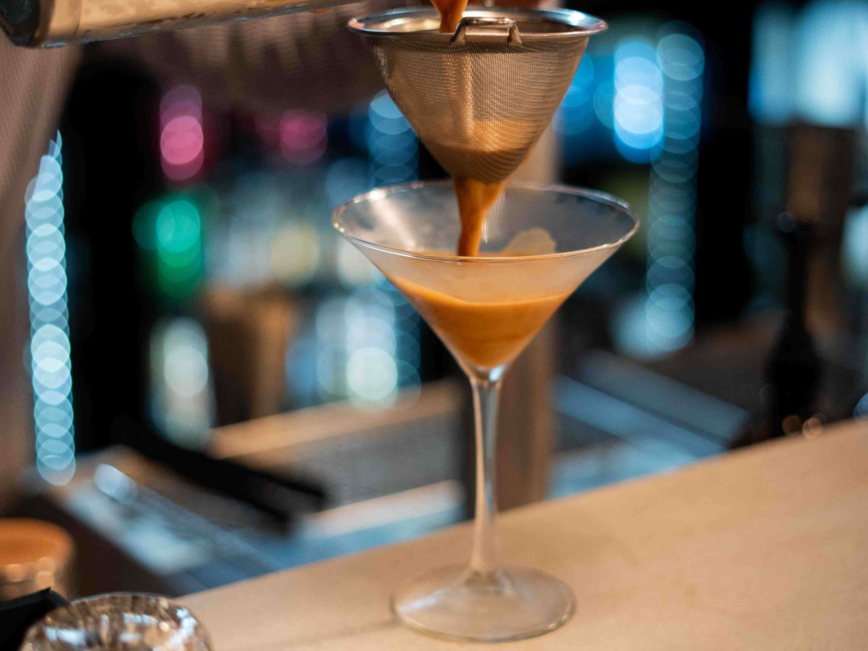A cocktail being poured into a martini glass.