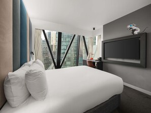 Habitación de hotel con cama, escritorio, silla, televisión y vistas a edificios.