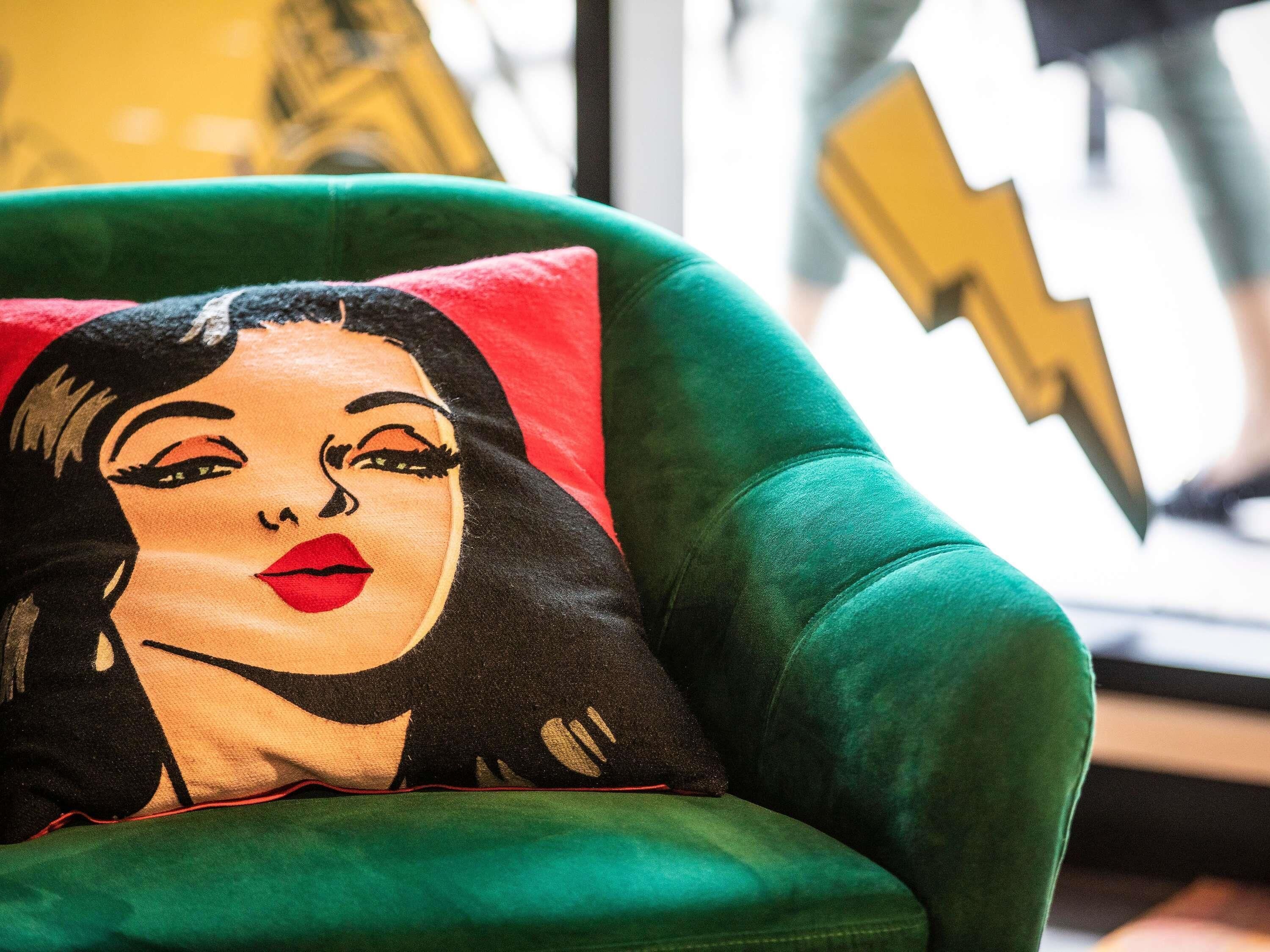 A green armchair with a pillow featuring a bold, graphic design.