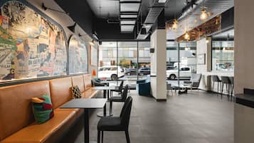 Un interior de cafetería moderno con asientos, un mural en la pared y vista a la calle.