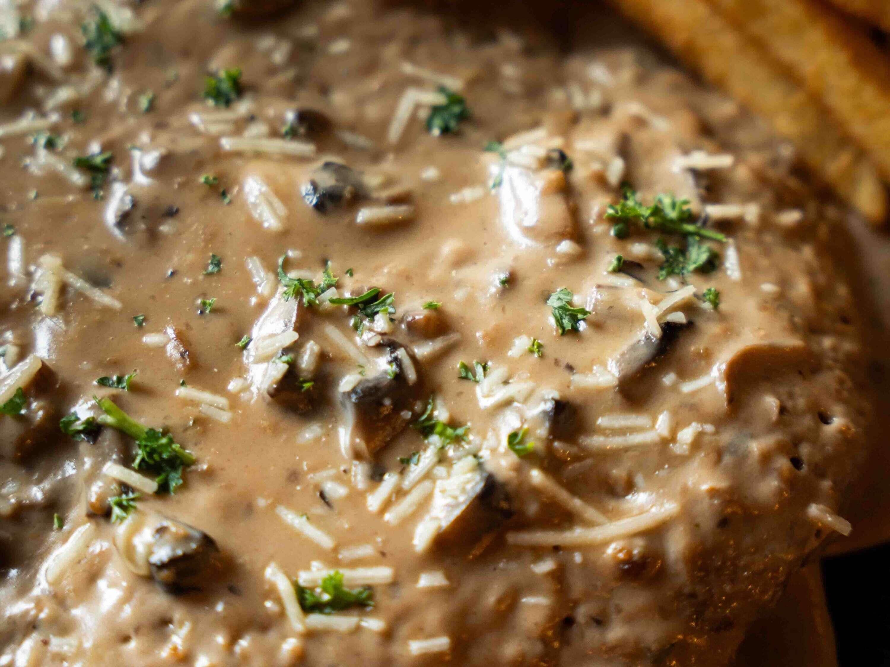 A close-up of a creamy mushroom dish with shredded cheese and parsley garnish.