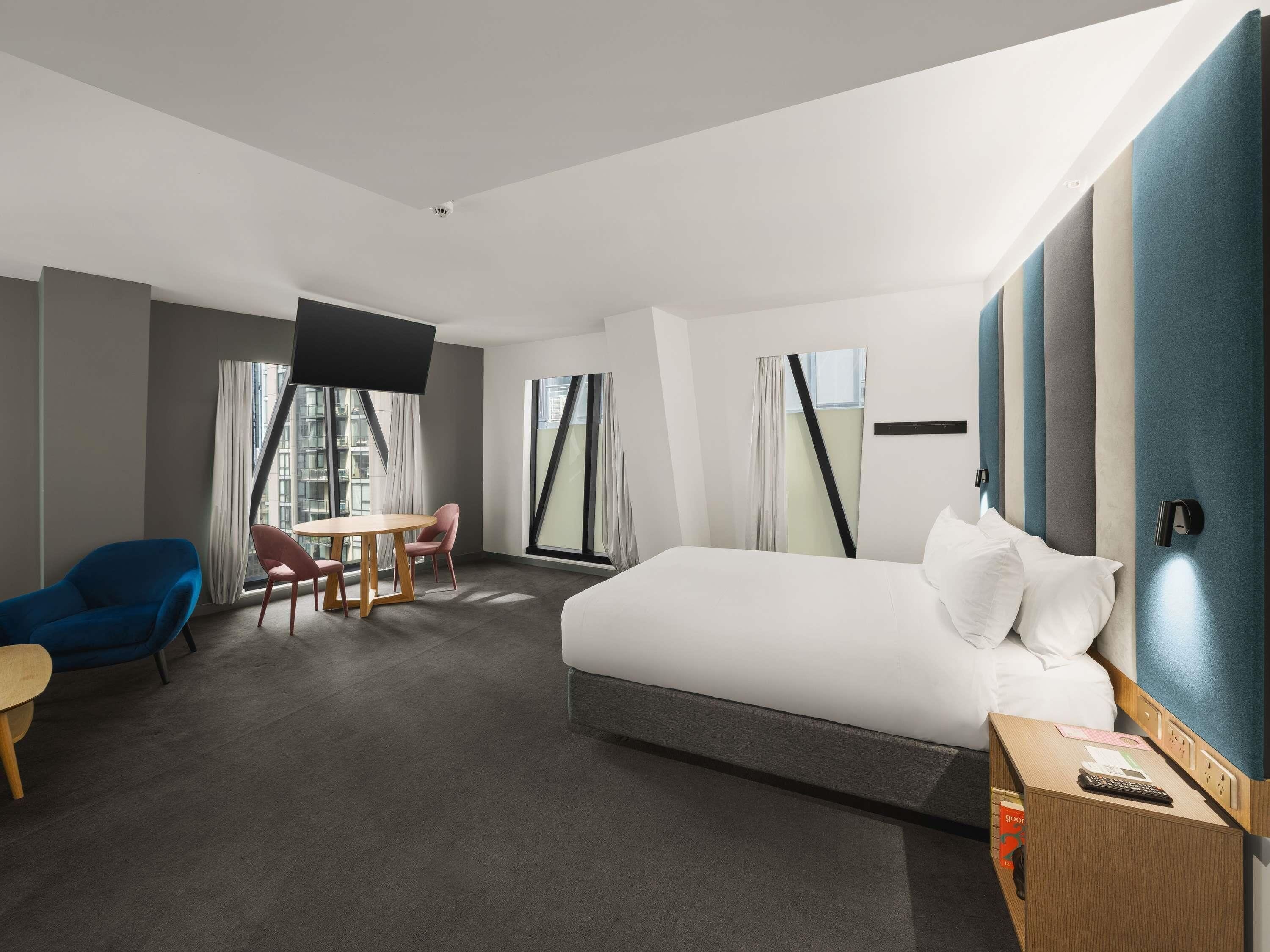 A hotel room with a bed, a desk with a chair, a TV, and a view of the city.