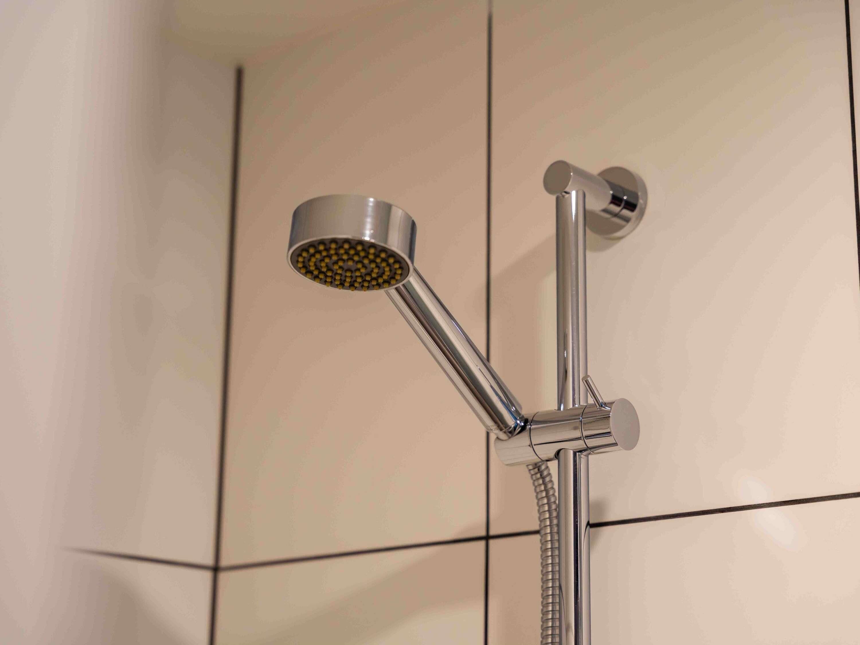 Un cabezal de ducha cromado con manguera flexible, fijado a una pared con azulejos.