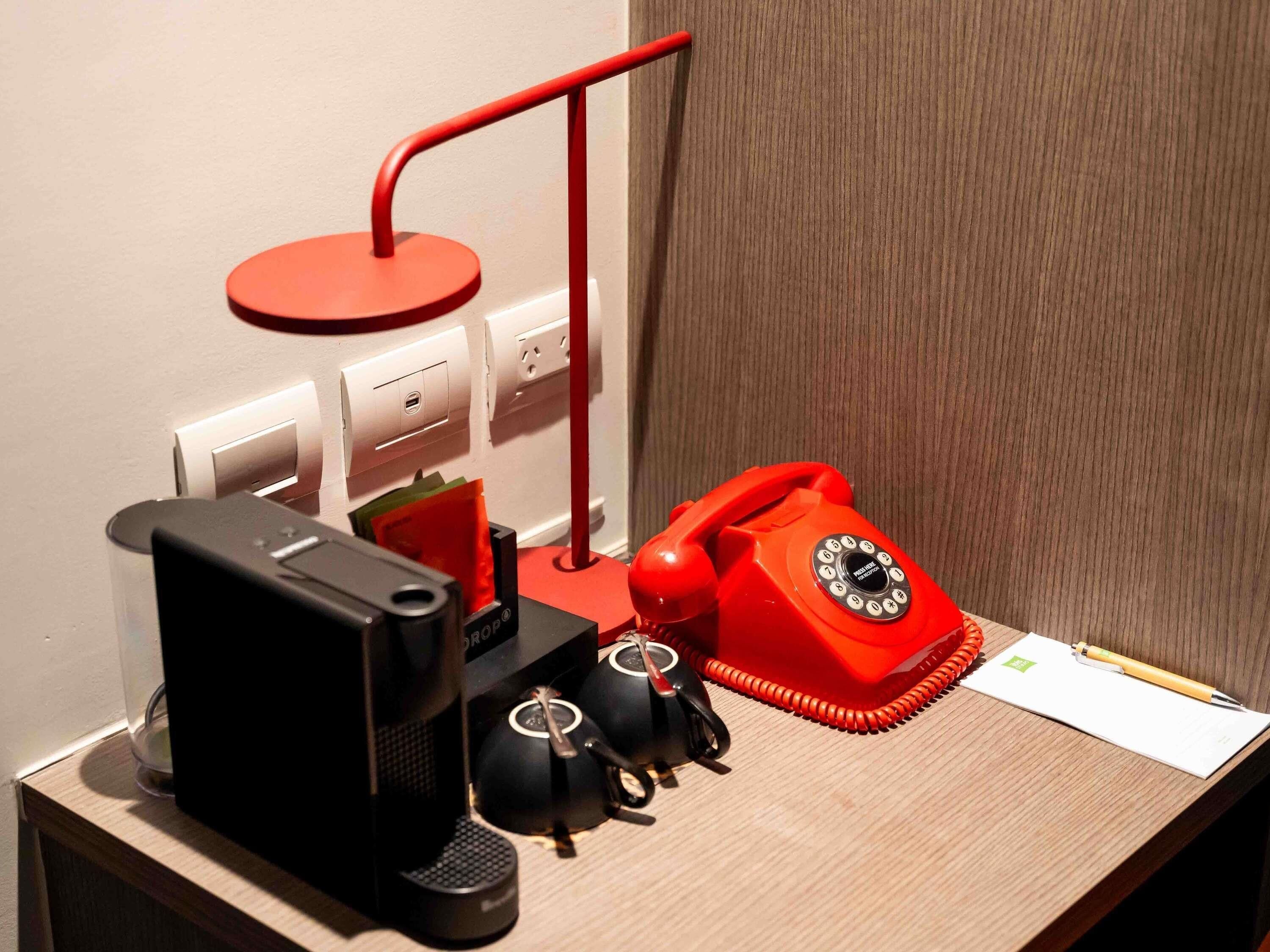 Een bureau met een rode draaischakel telefoon, een zwarte koffiemachine en een rode bureaulamp.